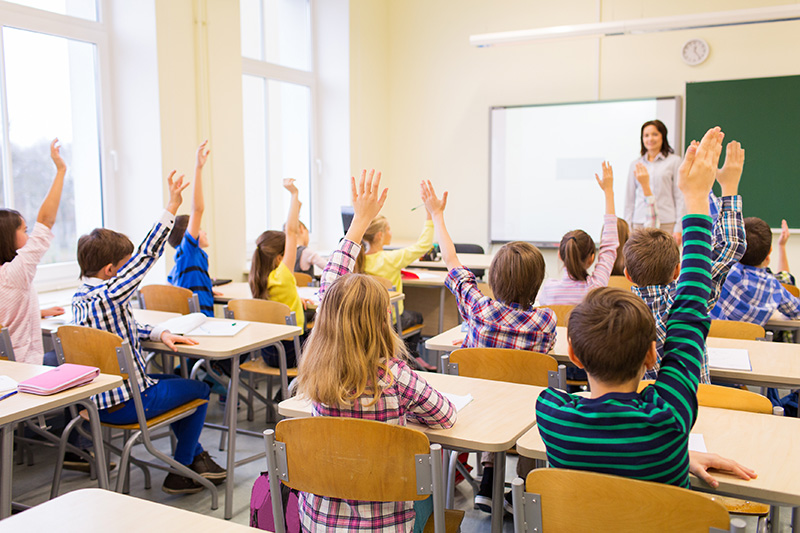 Group of school kids raising hands in classroom.