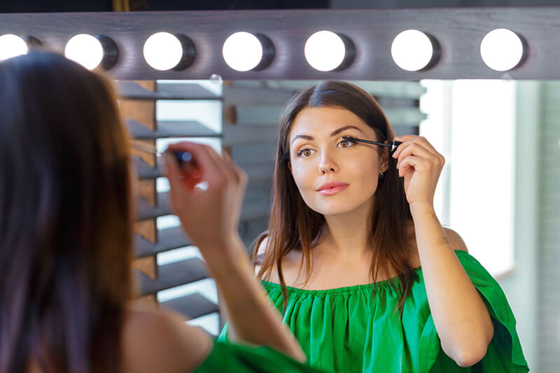 an image of a woman applying mascara in the mirror