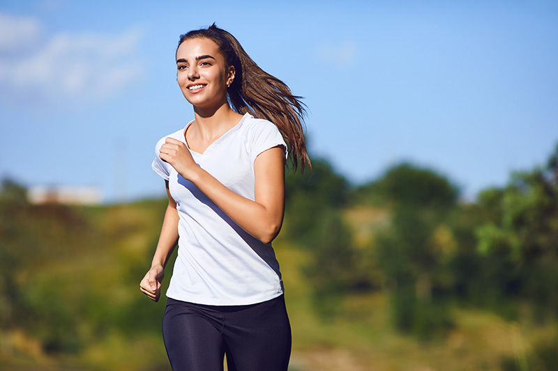 Woman running outside in an outdoor setting, wearing athletic clothing and enjoying physical activity.