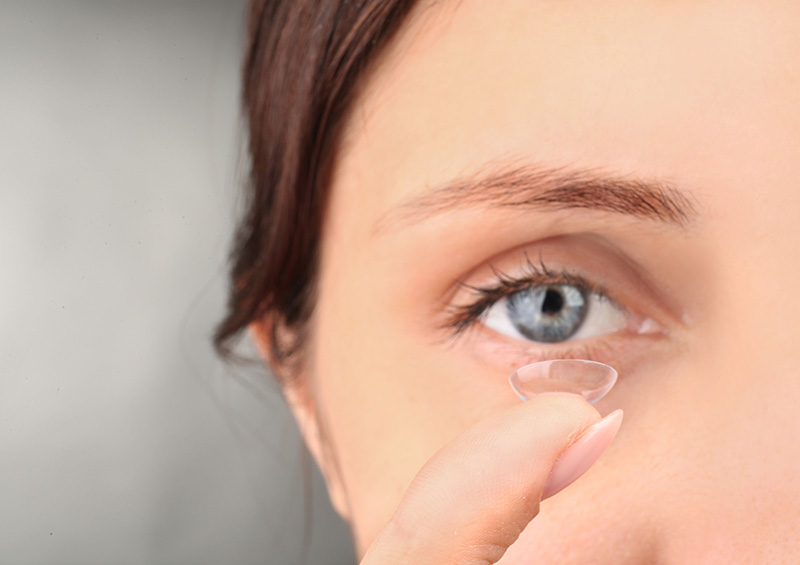 Young woman carefully placing a contact lens on her fingertip, preparing to insert it into her eye.